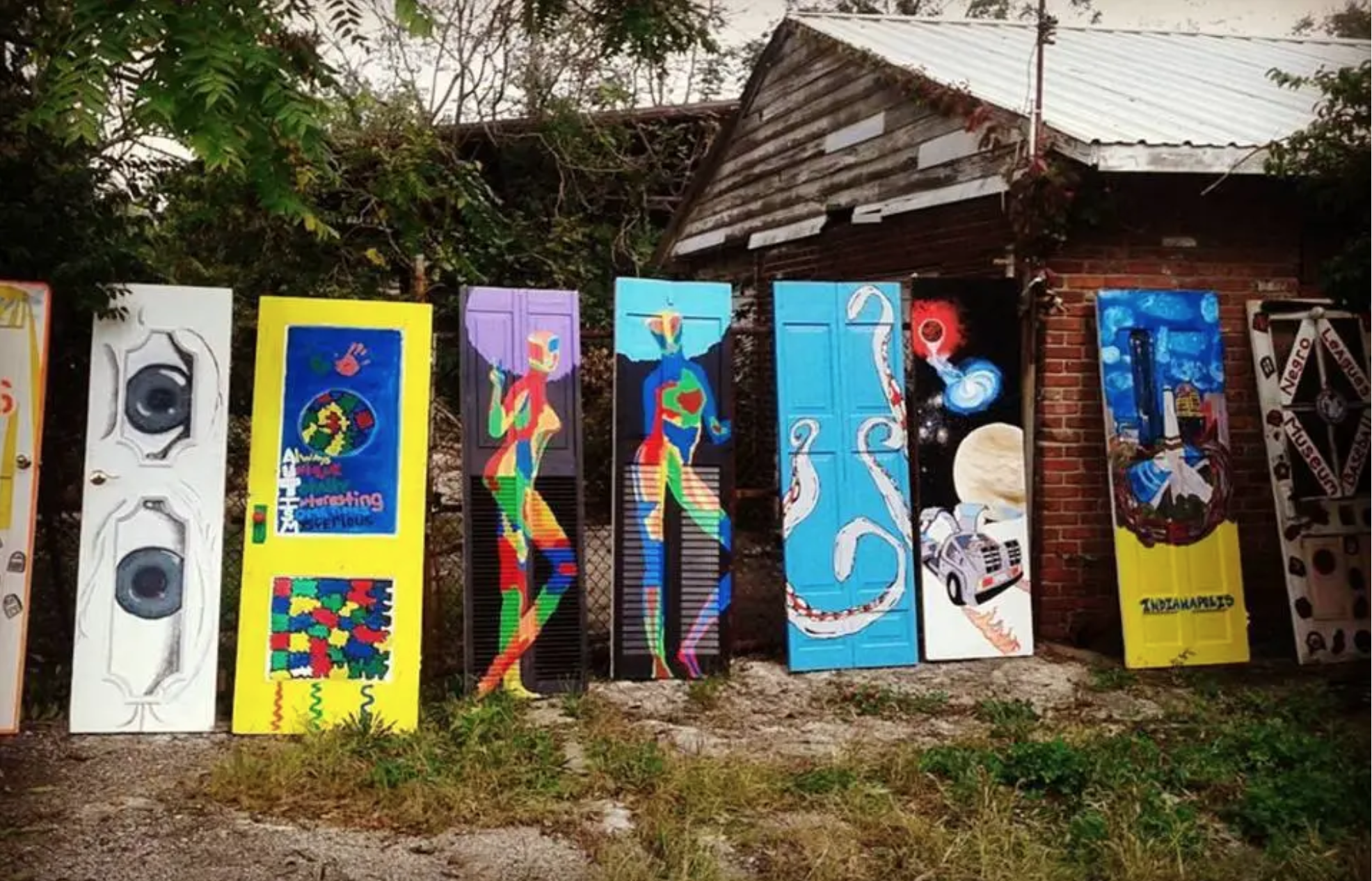 Brightly colored images of folk art on a collection of doors lined up along a fence