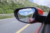 Red car driving forward looking at road ahead and image of road behind in the rearview mirror