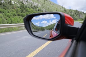 Red car driving forward looking at road ahead and image of road behind in the rearview mirror